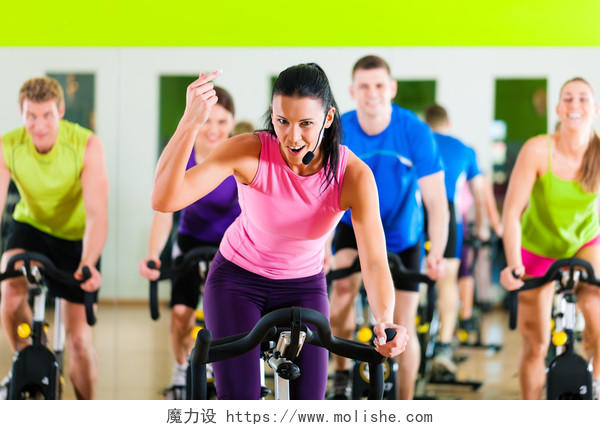 健身房教练在前面带领一群男人和女人锻炼他们的腿做有氧运动训练动感单车健身单车
